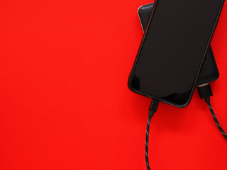  The smartphone is charging the power bank on a red background. Top view, there is space for text...