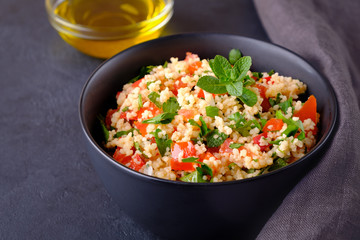 Tabbouleh salad in black bowl on black stone surface