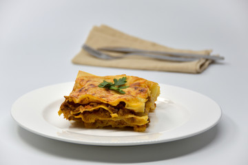 A piece of lasagna on a white plate. White background.