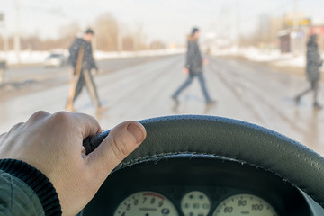 view from the car, a driver hand on the steering wheel of a car located in front of a pedestrian...