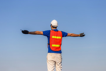 Successful young man with arms wide open, Happy engineer / foreman in hardhat and safety vest talks over blue sky background