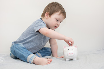 Fototapeta na wymiar a small cute child sits and puts coins in the piggy Bank. a child learns to save money.