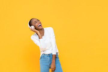 Happy African American woman laughing while listening to music on wireless headphone isolated on...
