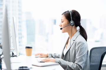 Young Asian businesswoman wearing headsets working in call center city office as a telemarketing...