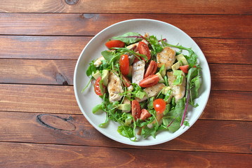 Chicken salad with avocado and cherry tomatoes, arugula and beet leaves. Healthy lunch bowl with vegetables and chicken on a wooden background. Healthy food concept