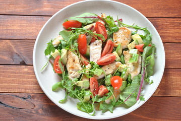 Chicken salad with avocado and cherry tomatoes, arugula and beet leaves. Healthy lunch bowl with vegetables and chicken on a wooden background. Healthy food concept