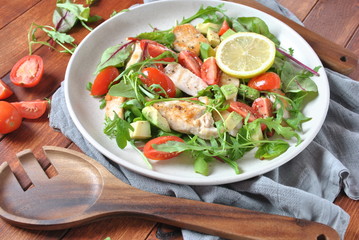 Chicken salad with avocado and cherry tomatoes, arugula and beet leaves. Healthy lunch bowl with vegetables and chicken on a wooden background. Healthy food concept