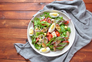 Chicken salad with avocado and cherry tomatoes, arugula and beet leaves. Healthy lunch bowl with vegetables and chicken on a wooden background. Healthy food concept