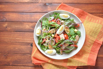 Chicken salad with avocado and cherry tomatoes, arugula and beet leaves. Healthy lunch bowl with vegetables and chicken on a wooden background. Healthy food concept