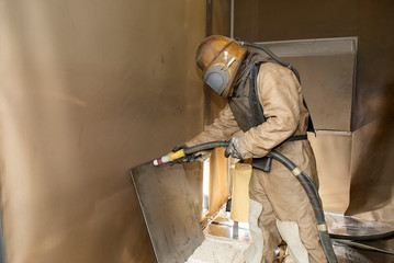 Man in protective clothing cleans industrially with high-pressure sandblasting 