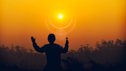 human holding christian cross and praying at sunset background. christian silhouette concept.