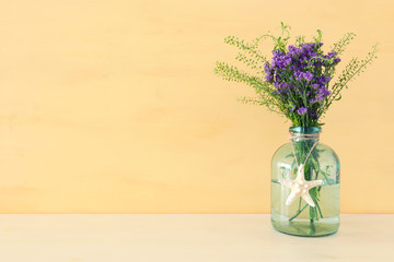 summer bouquet of purple field flowers in the nautical vase with seashell over wooden table and pastel old background