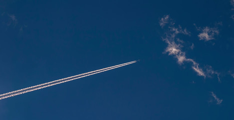 Airplane with contrail against blue sky and clouds