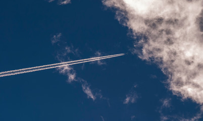 Airplane with contrail against blue sky and clouds