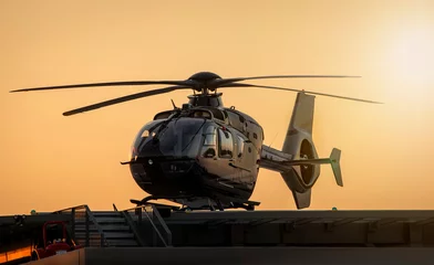 Rolgordijnen Zwarte helikopter vastgebonden op platform bij zonsondergang © F Armstrong Photo