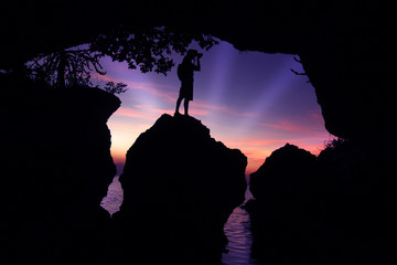 Photographer in front of the cave by the sea at sunset