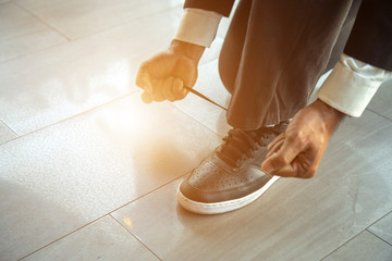 Close up body part of a man using his hands to tying up his shoelaces while sitting on floor