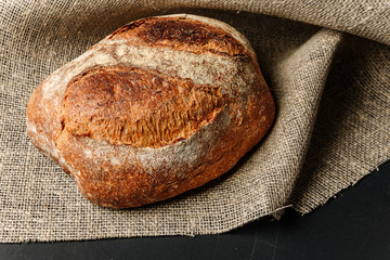 A loaf of dark bread lies on a canvas of burlap.