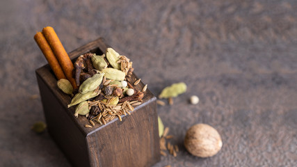 Garam masala, mix of different spices black and white peppercorns, cloves, cinnamon, mace, cardamom, cumin. Indian blend of ground spices in wooden box for cooking and Ayurvedic medicine.