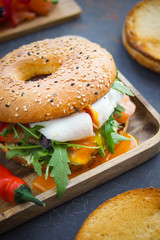 Bagel with salmon and poached egg on wooden board, Dark background, Breakfast bun