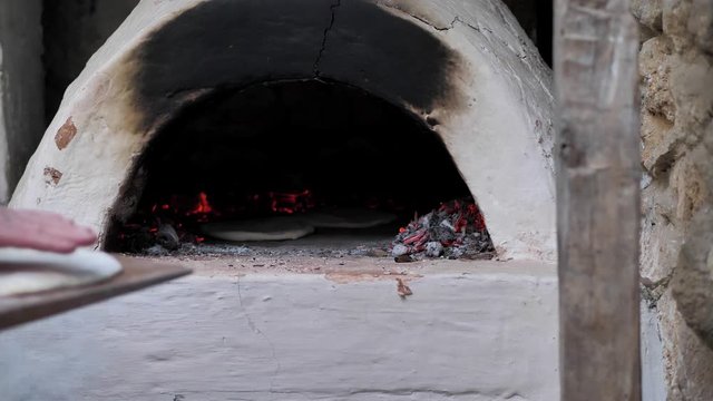 The man put the raw flatbread on a wooden spatula and put it in the oven.