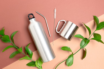 Green leaves, bottle, metal tube and cleaning brush. Zero waste accessories for drinking on brown...