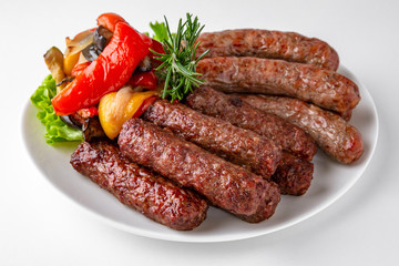 Grilled pork and beef sausages with vegetables. Banquet festive dishes. Gourmet restaurant menu. White background.