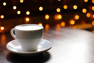 A cup of coffee on wooden table. Lights on the background. Front view.