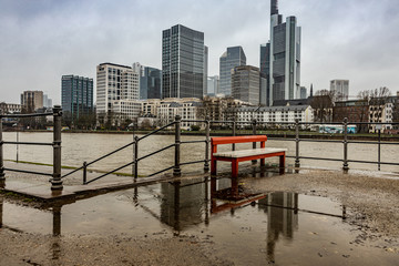 Fototapeta na wymiar Spiegelung Bank in Regenpfütze vor Frankfurter Skyline 
