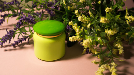 Green jar with cream on a pink background in a bouquet of flowers.  Mock up cream jars.  Hard shadow.  Beauty and personal care concept.