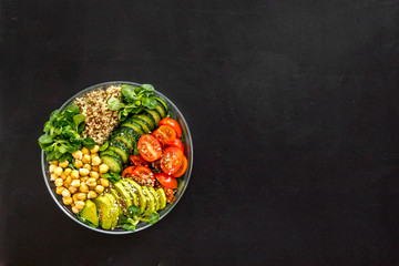 Fototapeta na wymiar Healhty vegan lunch bowl. Avocado, quinoa, sweet potato, tomato, spinach and chickpeas vegetables salad on black table. Top view
