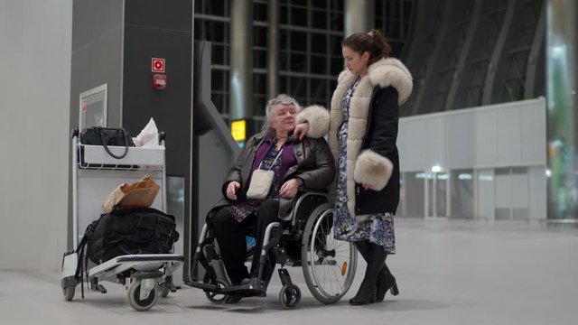 Wheelchair service in airport terminal, disabled person sitting in wheelchair, elderly woman with a family waiting for departure.