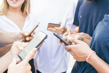 Group of friends meeting outside and using smartphones. Hands of men and women standing in circle and holding mobile phones. Mobile communication concept