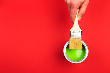 hand holding Brush  on open can of   paint on red  background. Renovation concept - Image