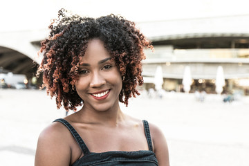 Happy cheerful African American lady posing in city square. Front portrait on young black woman...