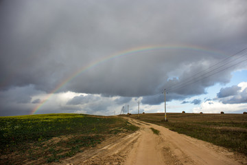 Rainbow against the background of clouds and a yellow field of rapeseed