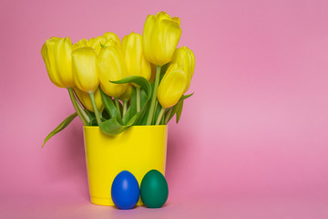 Spring bouquet of yellow tulips and easter painted eggs on pink background. Creative holiday backdrop