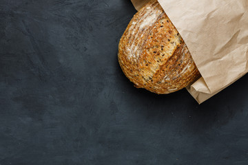 Fresh baked rustic bread loaf in paper bag. Artisan bread with seeds on dark table. Rustic...