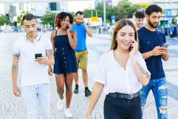 Happy excited woman talking on cell while walking down city street. Mix raced men and women going outside, talking on cells, using mobile phones. Smartphone using concept