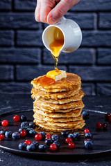 woman pouring honey on a stack of pancakes