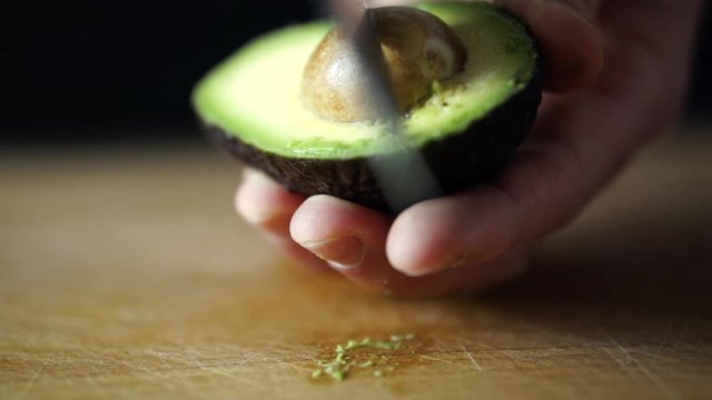 Caucasian male hand holding halved avocado and taking out its pit with sharp chefs knife, SLOW MOTION