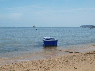 Fototapeta na wymiar Lonely small boat off the coast in the water. Sea, sand, horizon. Blue old plastic boat in the shallow water. Expanse of seawater and panorama of horizon. Seascape and sandy empty shore. 
