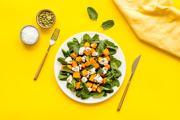 Light dish for lunch. Salad with pumpkin and basil on yellow background top-down