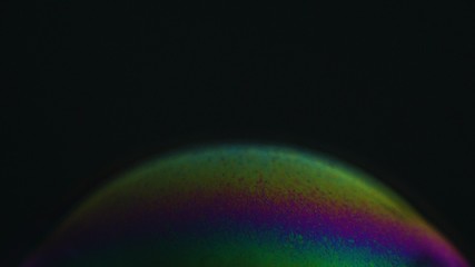 Rainbow soap bubble on a dark background. Close-up of colorful surface