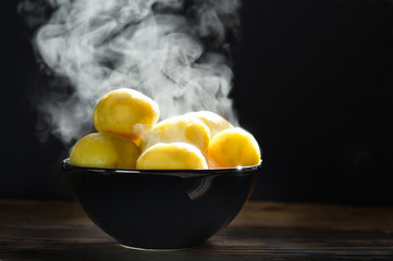 Steaming of boiled hot potatoes  in a black  bowl and butter served on wooden table ready to eat. 