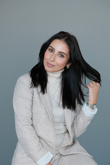 Obraz premium Portrait of a smiling mid-aged business woman in a light milk-colored trouser suit and turtleneck against a light wall.