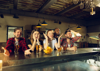 Sport fans cheering at bar, pub and drinking beer while championship, competition is going. Multiethnic group of friends excited watching translation. Human emotions, expression, supporting concept.