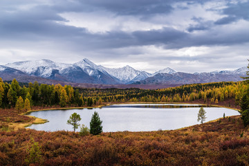 View of the Kidelu Lake and the snow-capped peaks of the Kurai ridge on the horizon. Autumn mountain landscape. Ulagansky District, Altai Republic, Russia