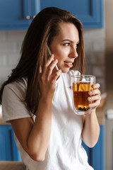 Image of pleased beautiful woman talking on cellphone and drinking tea