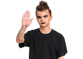Fototapeta premium Teen boy with spooking make-up doing stop sign with palm of hand, isolated on white background. Teenager in style of punk goth dressed in black making stop gesture with serious facial expression.